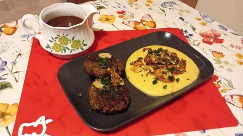Ein schwarzes Teller zeigt Kartoffel-Sellerie-Püree neben saftigen Hackfleischbällchen, umgeben von einer bunten Tischdecke.