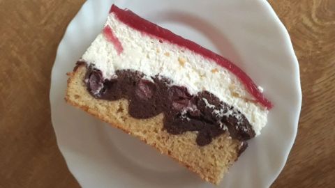 Ein Stück Schneewittchentorte mit Sauerkirschen liegt auf einem weißen Teller, hübsch dekoriert mit Sahne und roter Gelee-Schicht.