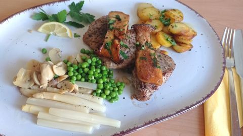 Saftiges Schweinefilet mit gebratenen Kräuterseitlingen und verschiedenen Gemüsebeilagen auf einem weißen Teller.