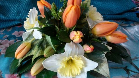 Ein hübsches Tischgesteck mit Frischblumen in sanften Farben, arrangiert auf einem blauen und floral gemusterten Hintergrund.
