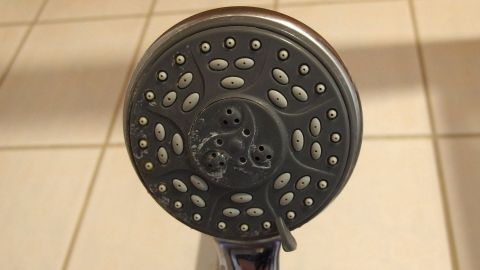 Der Brausekopf ist durch Kalkablagerungen grau gefärbt, während er in einer eleganten Badezimmerumgebung befestigt ist.