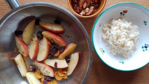 Karamellisierte Äpfel und Trockenfrüchte werden in einer Pfanne zubereitet, neben einer Schüssel mit Hirse und Walnüssen.