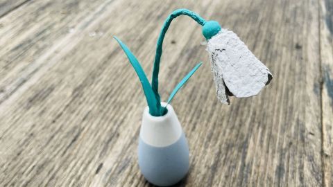 Ein Schneeglöckchen aus Eierkarton steht in einer Vase und zeigt Blüten und Blätter, umgeben von einer Holzoberfläche.