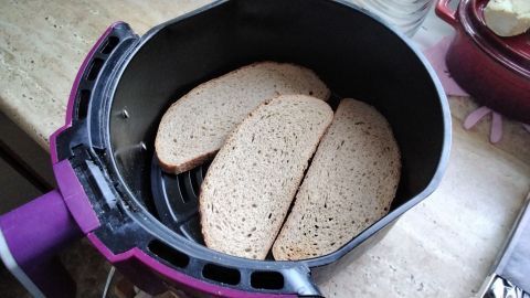 Scheiben Brot liegen in einer Heißluftfritteuse und warten darauf, geröstet zu werden, auf einer Küchenarbeitsplatte.