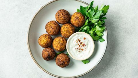Kugelförmige Falafel liegen auf einem Teller, umgeben von frischem Grün und einer Schale mit Dip.