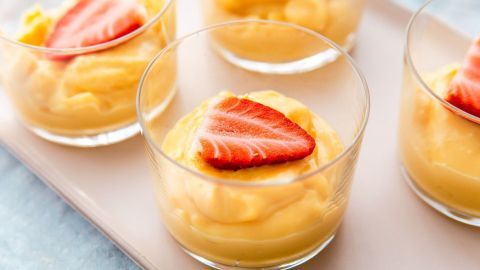 Kleine Gläser mit cremigem Vanillepudding sind dekoriert mit frischen Erdbeeren, auf einer hellen Platte präsentiert.