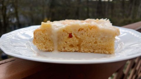Ein Stück Streuselkuchen mit Eierlikör liegt auf einem weißen Teller, in natürlicher Umgebung mit Bäumen im Hintergrund.