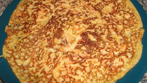 Auf einem blauen Teller liegen goldbraune Möhren-Pfannkuchen mit Käse, die eben frisch zubereitet wurden.