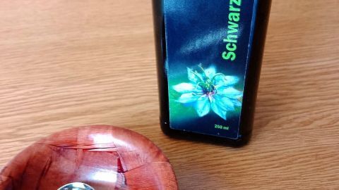 Ein Löffel mit schwarzkümmelöl liegt in einer Holzschale neben einer Flasche des Öls auf einem Tisch.