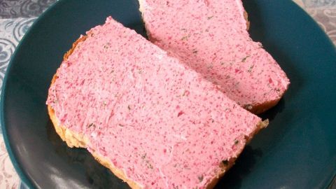 Zwei Scheiben Brot liegen auf einem Teller und sind dick mit Rote-Bete-Frischkäse-Butter bestrichen, appetitlich rosa.