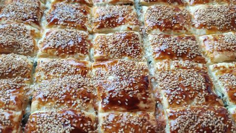 Käse-Schinken-Blätterteig-Snacks sind goldbraun gebacken, quadratisch geschnitten und mit Sesam bestreut.