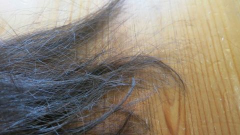 Haarspitzen mit Feuchtigkeitscreme pflegen: Einfach eine haselnussgroße Portion in die Haarspitzen einmassieren und durchkämmen. Verwirrte Haarspitzen liegen auf einer Holzoberfläche, die Feuchtigkeits-Körpercreme zur Pflege benötigt.