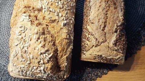 Ein frisch gebackenes Vollkornbrot mit Sesam auf einem Tisch, umgeben von einem runden Platzset und einer Orchidee.