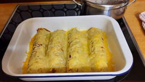 Im Auflaufform liegen einige mit Käse überbackene Rollen, umgeben von einer modernen Küchenumgebung.