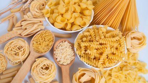 Vielfältige italienische Nudelsorten sind in Schalen und auf Löffeln arrangiert, umgeben von Weizenähren.