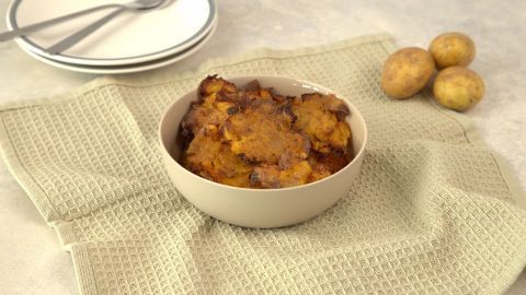 Geröstete Quetschkartoffeln liegen in einer Schüssel auf einem Küchenhandtuch, umgeben von frischen Kartoffeln.