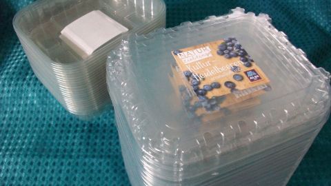 Kunststoffschalen für Obst stehen gestapelt auf einem blauen Tuch, bereit zur Wiederverwendung.