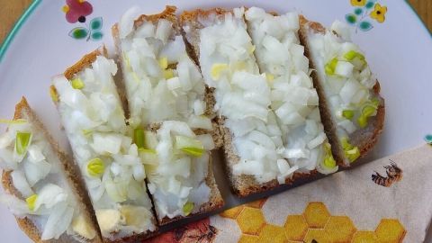 Auf einem Teller liegt frisch geschnittenes Schmalzbrot mit Zwiebeln, begleitet von einer bunten Serviette.