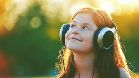 Ein Mädchen mit Kopfhörern hört Musik, strahlt Freude aus und genießt den idyllischen Sonnenuntergang im Hintergrund.
