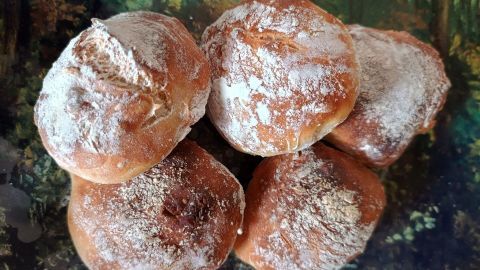 Sechs frisch gebackene Brötchen liegen auf einer rustikalen Unterlage, leicht mit Mehl bestäubt und appetitlich.