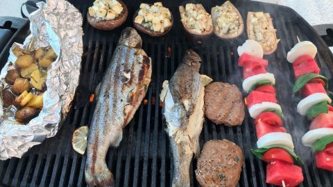 Auf dem Grill brutzeln frischer Fisch und Gemüse. Der Rauch steigt auf, während die Grillgerichte für ein Fest bereit sind.