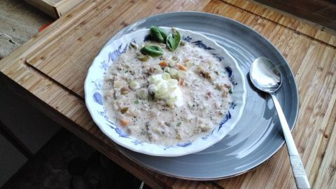 Cremige Gemüsesuppe wird in einer tiefen Schüssel serviert, umgeben von frischen Kräutern auf einem Holztisch.