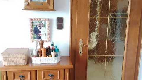 Ein Holzschrank und eine Holztür stehen in einem Raum. Der Schrank ist dekorativ mit Geschirr und Pflegeprodukten gefüllt.