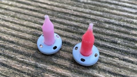 Zwei Mini-Kerzenständer stehen auf einem Holzuntergrund, jeder mit einer bunten Kerze in der Mitte.