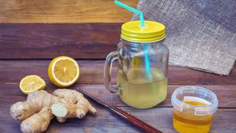 Ein Glas mit Switchel steht auf einem Holztisch neben ingwer, Zitronen und Honig, bereit zum Genießen.