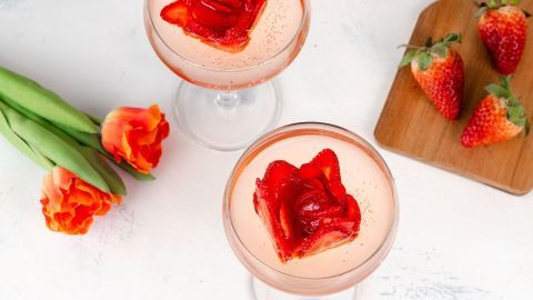 Rosen-Eiswürfel aus Erdbeeren liegen in eleganten Gläsern mit süßem Getränk, umgeben von bunten Tulpen und frischen Erdbeeren.