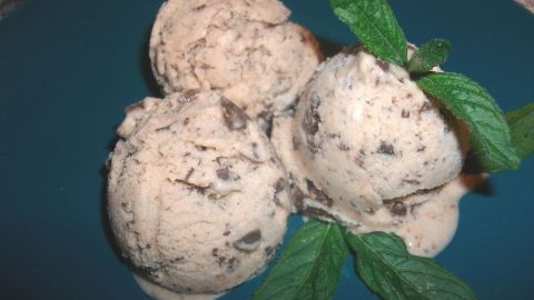 Drei Kugeln Bananen-Schoko-Eis liegen auf einem blauen Teller, umgeben von frischen Minzblättern.