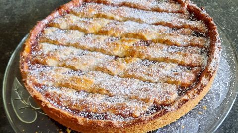 Eine Linzer Torte mit Puderzucker bestäubt liegt auf einer gläsernen Platte und entfaltet ihr goldenes Aroma in einer eleganten Küche.