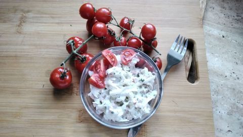 Ein frischer Rettichsalat mit Tomaten liegt in einer Schüssel, umgeben von einer Traube saftiger Kirschtomaten auf einem Holzbrett.