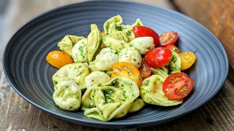 Ein schwarzer Teller mit Tortelloni, die mit Pesto und bunten Cherry-Tomaten garniert sind, auf einem rustikalen Tisch.