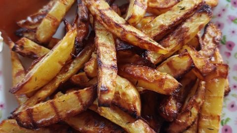 Knusprige Pommes aus frischen Kartoffeln liegen auf einem Teller mit Blümchenmuster und werden von einer Sauce begleitet.