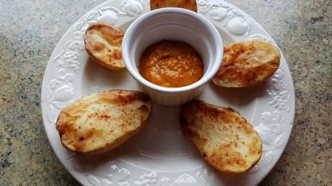 Auf einem weißen Teller liegen gebackene Kartoffeln um eine Schüssel mit Chutney, die zum Dippen einlädt.