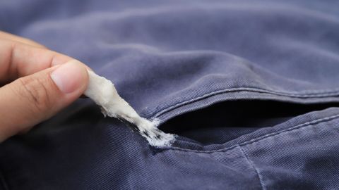 Ein Finger hält Kaugummi, der aus einem blauen Textil gezogen wird; der Stoff ist sichtbar verknittert und unordentlich.