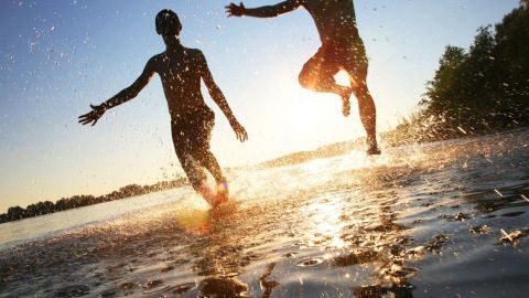 Zwei Kinder springen fröhlich ins Wasser, während die Sonne untergeht, und versprühen dabei spritzige Wassertropfen im Sommerurlaub.