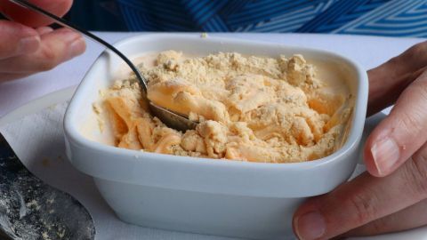 Ein Löffel gräbt in einer cremigen Gofio-Mousse, während eine Hand die Schüssel festhält, umgeben von einem gedeckten Tisch.