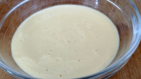 Eine glatte, cremige Mayonnaise aus gekochtem Ei befindet sich in einer Glasschüssel auf einem Holzbrett.