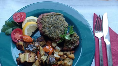 Ein köstliches Thunfischsteak mit Kräuter-Topping ruht auf einem blauen Teller, umgeben von buntem Gemüse und Zitrone.