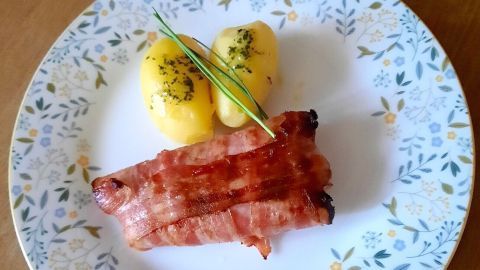 Auf einem gedeckten Teller liegen zarte Spargelpäckchen und Kartoffeln, garniert mit Schnittlauch.