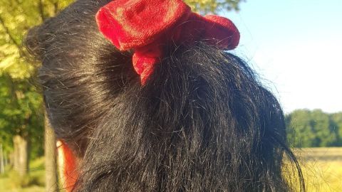Dunkles, lockiges Haar wird von einer Person mit einem roten Haargummi im Freien getragen, umgeben von Natur.