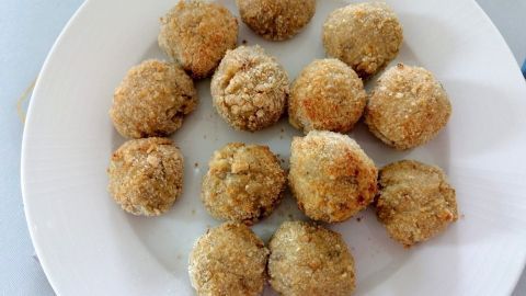 Frittierte spanische Kroketten mit Schinken liegen knusprig auf einem weißen Teller, umgeben von einer hellen Tischoberfläche.