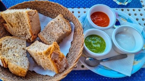 Brotscheiben liegen in einem geflochtenen Korb, daneben befinden sich drei Schalen mit verschiedenen Dips für den Tapas-Abend.