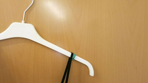 Trägerkleider rutschen vom Bügel? Es passiert nicht mehr so leicht, wenn man Gummis um die Bügelenden wickelt. Ein Kleiderbügel hält ein Trägerkleid mit einem Gummiband, um ein Herunterrutschen zu verhindern, vor einer Holzoberfläche.
