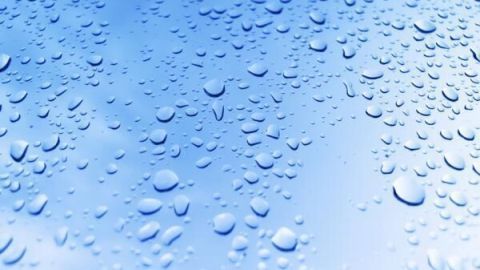 Wassertropfen bilden sich auf einer glatten Oberfläche, die mit Autowachs versiegelt wurde, glitzernd im blauen Licht.