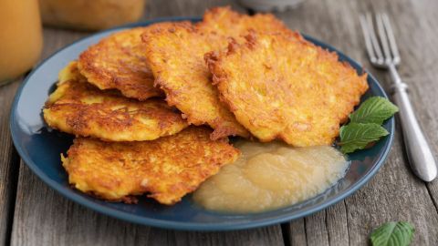 Goldene Kartoffelpuffer liegen auf einem blauen Teller, serviert mit Apfelmus und frischen Minzblättern.
