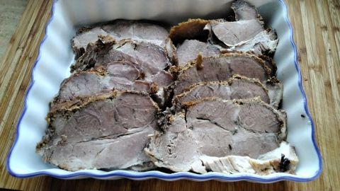 Saftiger Schweinebraten mit Senfkruste liegt in einer weißen Auflaufform auf einer Holzunterlage.
