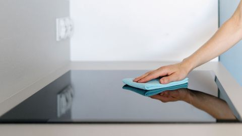 Ein Hand wischt mit einem blauen Tuch über ein glänzendes Ceranfeld in einer modernen Küchenumgebung.